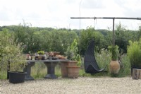 Decorated area at the terrace with gravel with recycled and vintage pots on stone table and hanging chair.