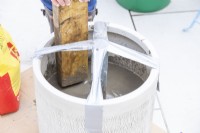 Woman using block of wood to tamp down cement