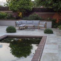 Reflection of illuminated tree at dusk in rectangular pool on terrace with garden furniture