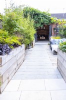 Staggered stone tile path leading towards summerhouse past wooden raised borders and bamboo