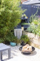 Firepit and water feature in corner of garden by raised bed, bamboo and various pot plants