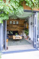 Wisteria growing over entrance to small summer house with pallet coffee table and sofa