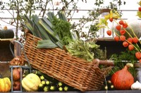 Display of harvested produce, including mixed winter squash and leeks in willow basket.