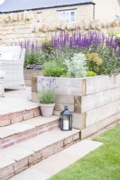 Lantern and a pot of Lavender on stone tile steps next to raised beds planted with Lavender, Salvia, Artemisia and Euphorbia