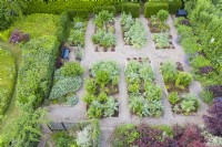 View over formal garden  with gravel paths and rectangular beds containing Cynara cardunculus and Heuchera backed by hedges of Yew. June. Summer. Image taken with drone. 