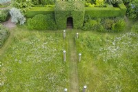View over meadow with formal avenue of cut grass lined with wooden posts topped with stainless steel globes. Border of Hydrangeas with hedge of Box and large clipped hornbeam entrance June. Summer. Image taken with drone. 