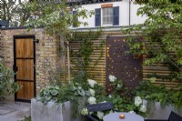 Courtyard garden at dusk with raised beds and contemporary wood boundary fence with back lit decorative metal screen near seating area