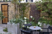 Courtyard garden at dusk with raised borders and contemporary wood boundary fence with metal screen and lighting