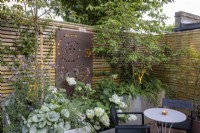 Courtyard garden at dusk with raised beds and contemporary wood boundary fence with metal screen and lighting