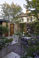 A paved courtyard garden with stone raised beds screening small seating area. Contemporary boundary comprising brickwork, fencing and a metal screen.