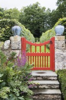 Red painted wooden gate from South Garden to House Field in stone wall with stone steps. August.