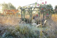 Wooden rustic gazebo and seats in frost surrounded by frosted
ornamental grasses 