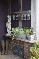 Front porch with wellington boots, candle lamps, a Greek Goddess statue, pet remembrance slate plaques and planted pots. 
