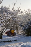 The garden at Gravetye Manor, Sussex, in winter. Gardener driving a small tractor through the orchard