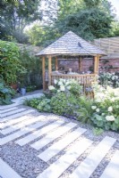 Mixed border separating staggered stone tile path from round wooden gazebo