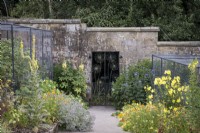 Ornate metal garden gate with Allium design and Hollyhock, Echinops and Evening Primrose in foreground