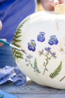 Woman painting glue over pressed flowers to stick them to the pumpkin