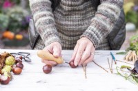 Woman using bradawl to poke two holes in each of the conkers