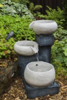 Cascading granite bowls water fountain in mulch border in backyard garden in summer.