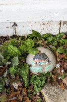 A pebble in a garden with a painted image of a cottage