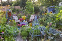 In front are vegetable beds with growing vegetables, and in the back garden furniture with a flower arrangement, a wooden gazebo and a bed with perennials.