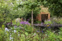 View across borders and an interactive water feature to the woodland retreat on the wheelchair accessible Horatio's Garden - Designers Hugo Bugg and Charlotte Harris, Harris Bugg Studio - RHS Chelsea Flower Show 2023