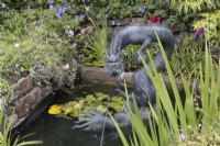 A large copper dragon sculpture, Chinese style, in a pond setting with a stream of water spraying from the mouth. Summer.