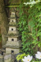 Home-made five tiered pagoda garden ornament made in cast concrete sections and placed in shady position next to fence clothed with Parthenocissus quinquefolia - Virginia creeper. July.