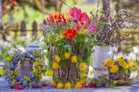 Bouquet of spring flowers including wildflowers and tulips in a vase covered with bark, wreaths made of dandelion flowers and Myosotis. Tea pot made of bark, willow and lichens filled with bouquet of dandelion and muscari.
