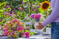 Woman arranging outdoor table with wreath and bouquet of flowers in a vase. Flowers in bouquet are Hydrangea, sweet peas, Ammi majus and Nigella while wreath is made of Clematis seed heads, Dahlia and Rudbeckia.