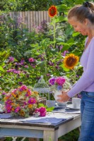 Woman arranging outdoor table with wreath and bouquet of flowers in a vase. Flowers in bouquet are Hydrangea, sweet peas, Ammi majus and Nigella while wreath is made of Clematis seed heads, Dahlia and Rudbeckia.
