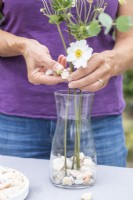 Woman placing stones in vase with white Anemones to hold them in place