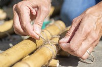 Woman tying shorter pieces of bamboo between two longer pieces to create a small ladder