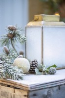 Bauble, pinecone, Ivy and Pine sprigs next to lantern with glass frosted over on wooden crate