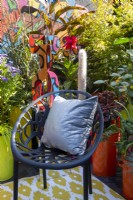 A modern contemporary colourful balcony terrace garden with black chair and cushion - container planting including Miscanthus sinensis 'Dronning Ingrid', Acer, Oreocereus leucotrichus - Old Man of the Andes and Hylotelephium 'Jose Aubergine' - Pop Street Garden RHS Chelsea flower Show September 2021 