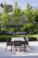 Dining table and chairs on pale paved patio in modern garden