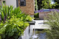 Running water from spout in raised metal flowerbed in modern garden