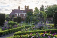 A Victorian walled garden has a central arbour, around which a formal arrangement of differently shaped, box edged beds emanate: planted with tulips, honesty, euphorbia and a sea of leafy perennials. Yew columns add permanence.