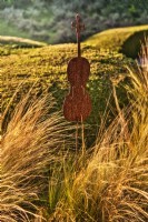 Mediterranean  garden view of zone near the entrance with grassland of Stipa tenuissima with violin sculpture in autumn time, sunlit with warm evening light.

Italy, Tuscan Maremma, Orbetello
Autumn season, October