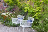 In the middle of the garden, two wirework chairs sit on a pebbled area, set against a backdrop of helenium, lythrum, white hydrangea and hardy geranium.