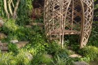 Stepping stones in a damp shady garden with a modern contemporary geodesic structure made from Moso bamboo with wooden bench seat 