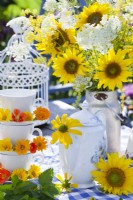 Table arrangement with a bouquet of sunflowers, teapot, self made stand of teacups and saucers decorated with pot marigold and nasturtium flowers.