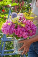 Woman holding vase filled with summer flowers including hydrangea, fennel, veronicastrum and echinops.