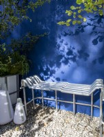 Repurposed upcycled modern contemporary metal bench seat made from an IBC - intermediate bulk container frame - on a gravel surface patio - blue painted rendered wall