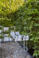 Repurposed upcycled modern contemporary metal bench seat made from an IBC - intermediate bulk container frame - on a gravel surface patio and a Carpinus betulus - Hornbeam hedge