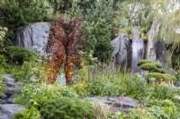 Metal sculpture by Penny Hardy in a rock garden a waterfall and mixed perennial planting of Pines, Willow, Bistorta amplexicaulis 'Atrosanguinea', Veronica longifolia, Chamomile, Achillea millefolium and cloud-pruned Pinus mugo 