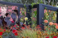 RHS COP26 Feature Garden with flowerbed planting of various dahlias including 'Bishop of Llandaff', Crocosmia 'Lucifer', ornamental grass and Canna x generalis Cannova Bronze Scarlet - black painted timber arbour 