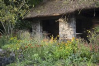 Old stone forge building with thatched roof - Malus - crab apple and mixed planting perennial border with Digitalis, Crocosmia, Coreopsis grandiflora, Echinacea, Kniphofia, Helenium and ornamental grasses 