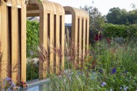 A modern contemporary wooden canopy pergola with water rills in to a pond - planting includes Miscanthus sinensis 'Red Chief'