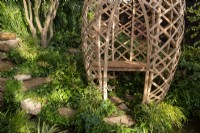 Stepping stones in a damp shady part of the garden leading down to a modern contemporary geodesic laminated lattice-work circular structure made from Moso bamboo - Phyllostachys edulis with a wooden bench seat